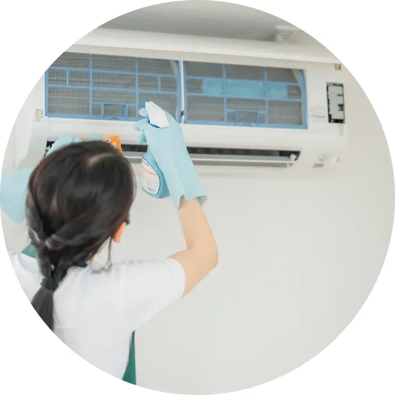 室内の壁掛けエアコンを、手袋をした女性がスプレーを使って清掃している様子