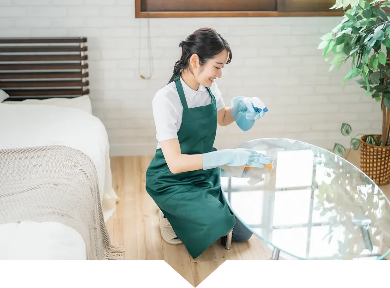 緑のエプロンを着た清掃スタッフがテーブルを拭いている様子