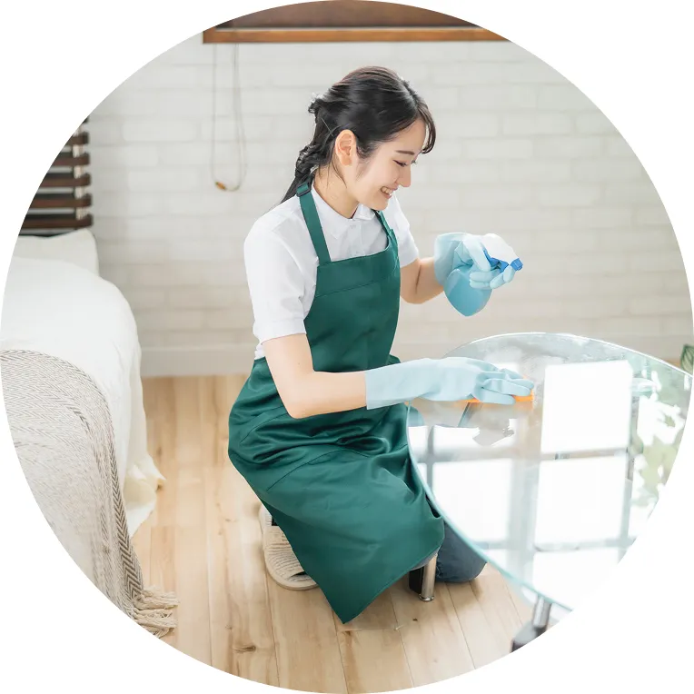 緑のエプロンを着た清掃スタッフがテーブルを拭いている様子