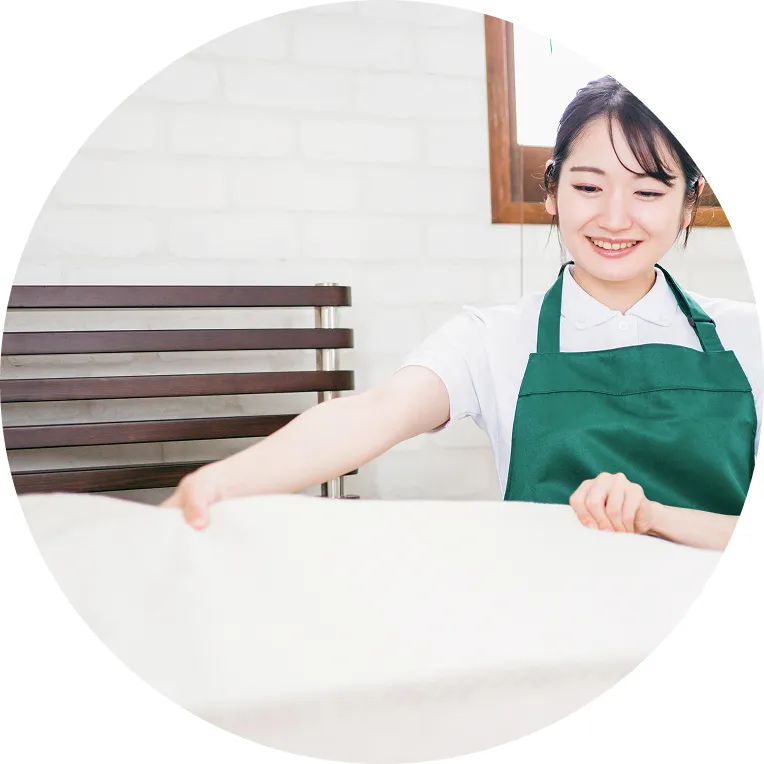 緑のエプロンを着たスタッフがシーツを広げている様子