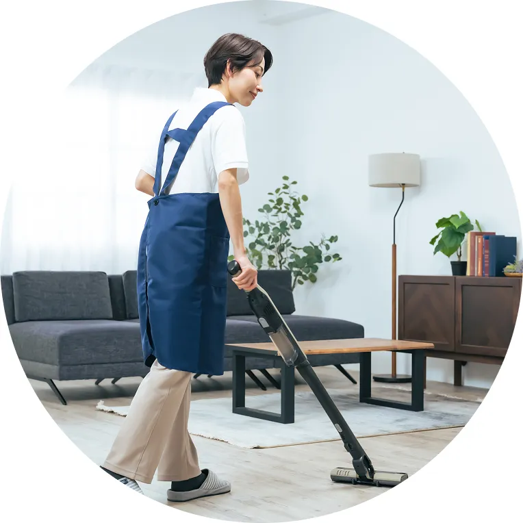 青いエプロンを着たスタッフが床を掃除機で清掃している様子